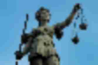 Bronze Lady Justice statue holding sword and scales against a blue sky, representing legal accountability