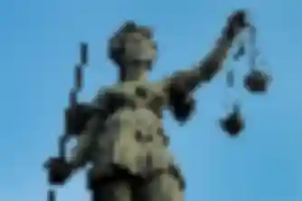 Bronze Lady Justice statue holding sword and scales against a blue sky, representing legal accountability
